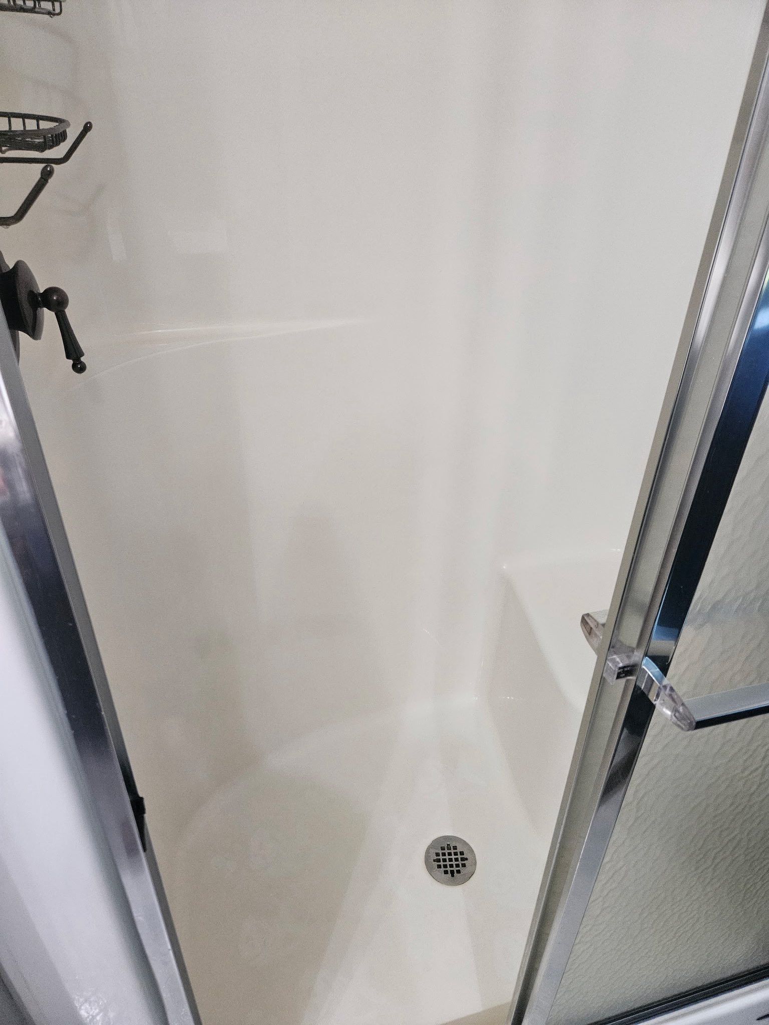 A white, walk-in shower enclosure with a built-in corner seat, chrome drain, and glass door.
