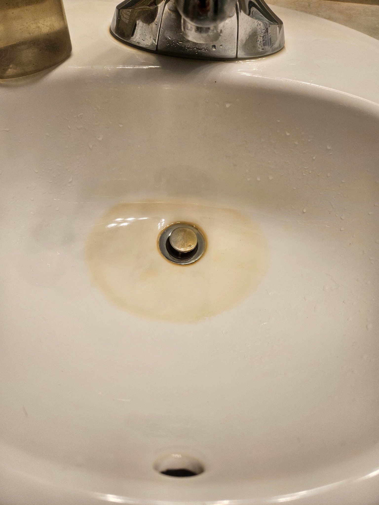 White bathroom sink with a round, orange-brown rust stain concentrated around the center drain.