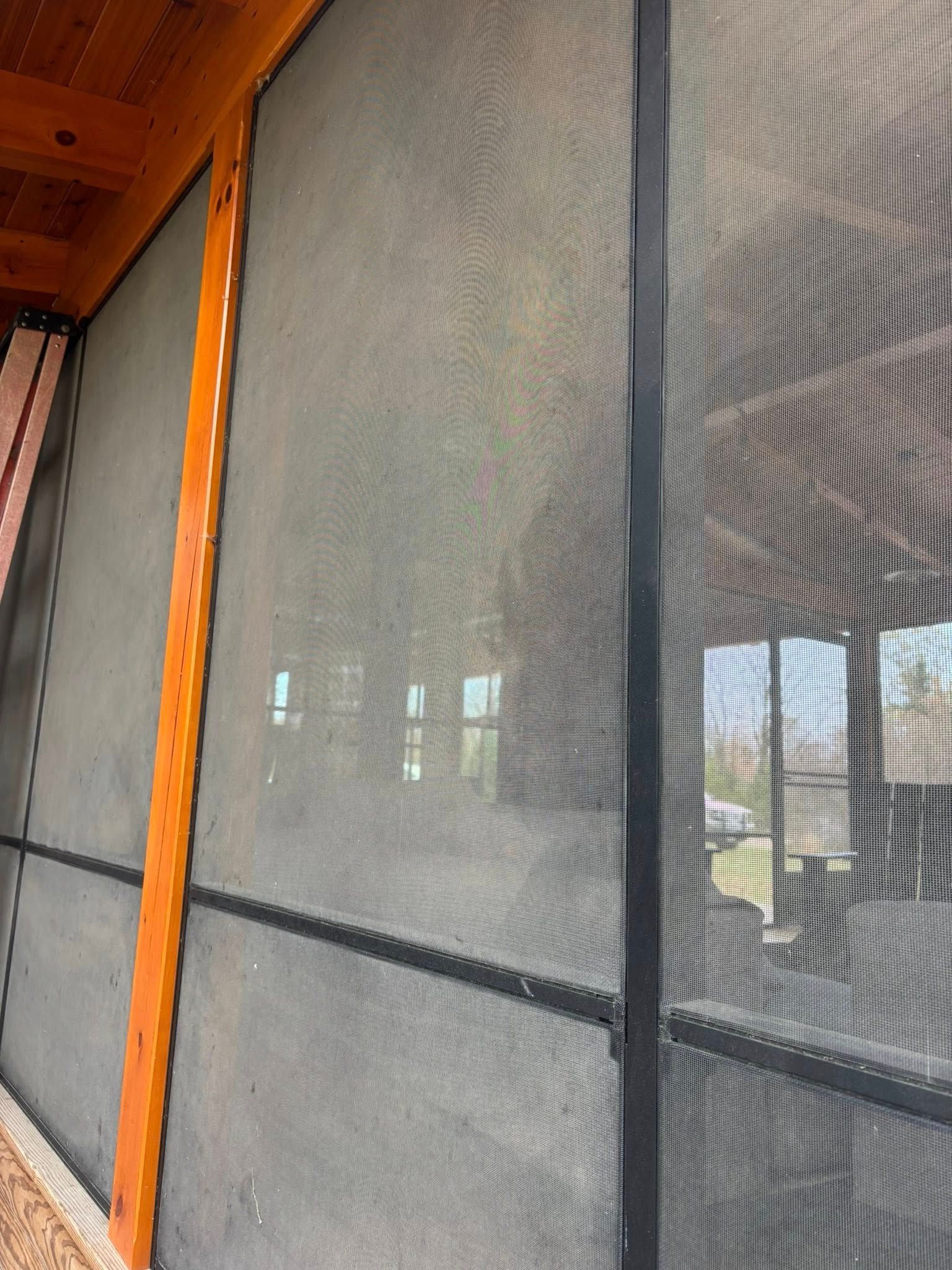 A screened-in porch with dark mesh panels separated by vertical wooden and black metal framing elements.
