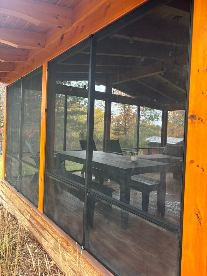 A wooden-framed screened-in porch with a dark table and bench set visible inside.
