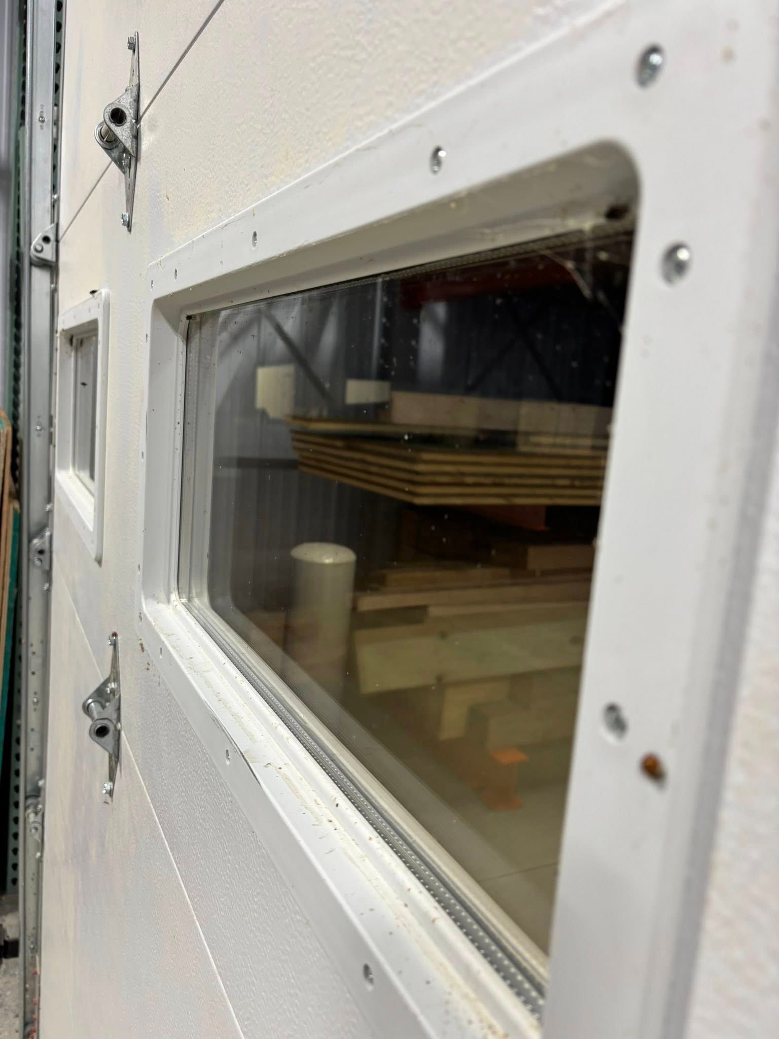 A close-up, angled view of a rectangular window insert mounted on a white garage door, showing stored materials inside.