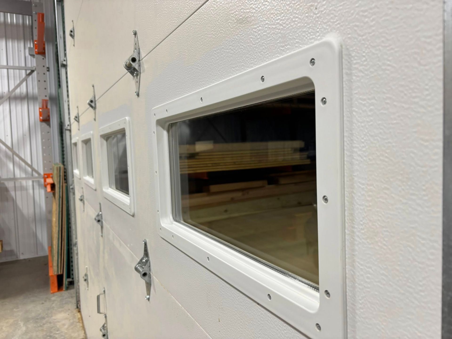 White garage door sections with rectangular windows installed in a warehouse setting.