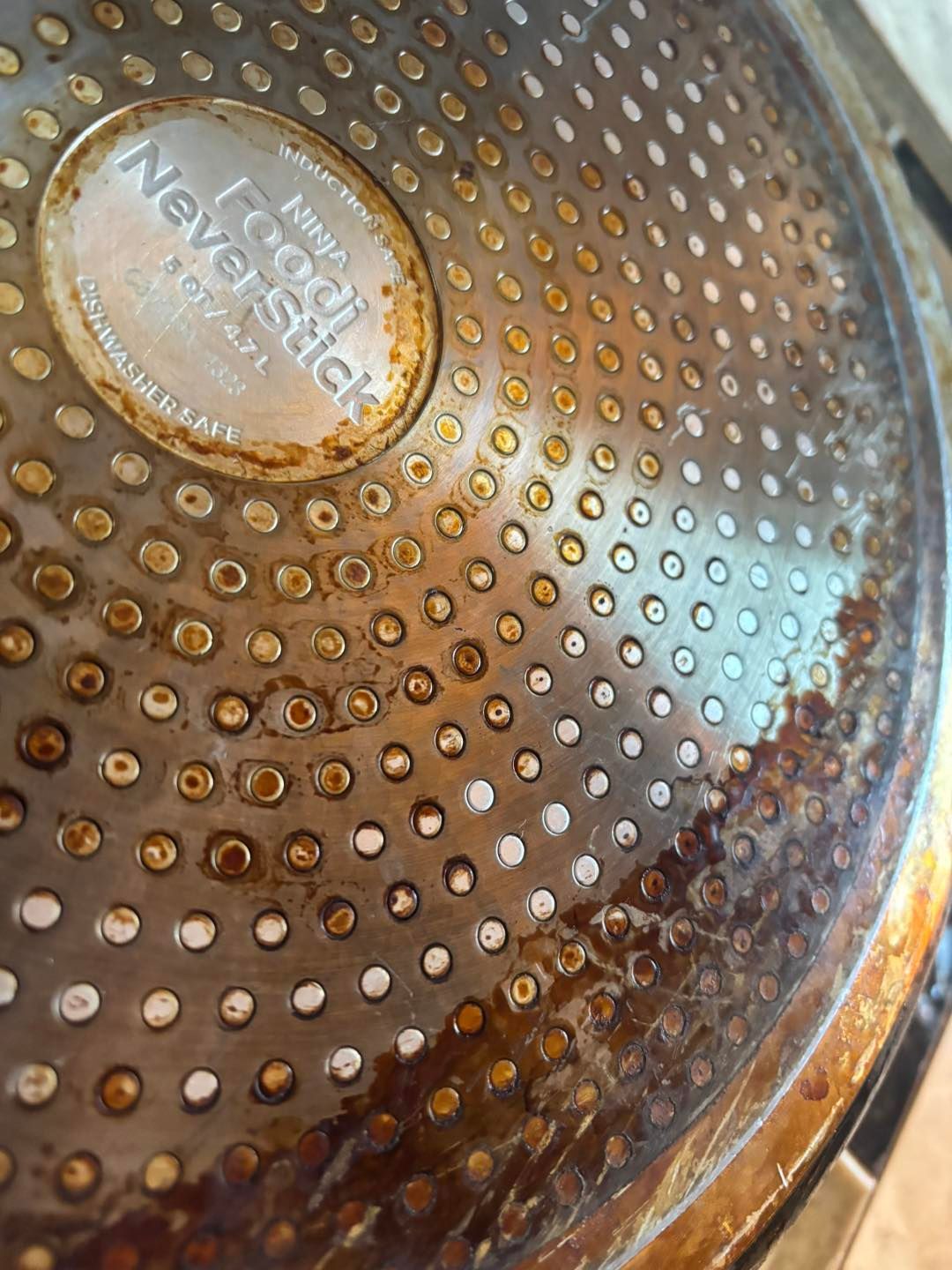 The underside of a Ninja Foodi NeverStick pan, showing heavy grease buildup and brown discoloration on the metal surface.
