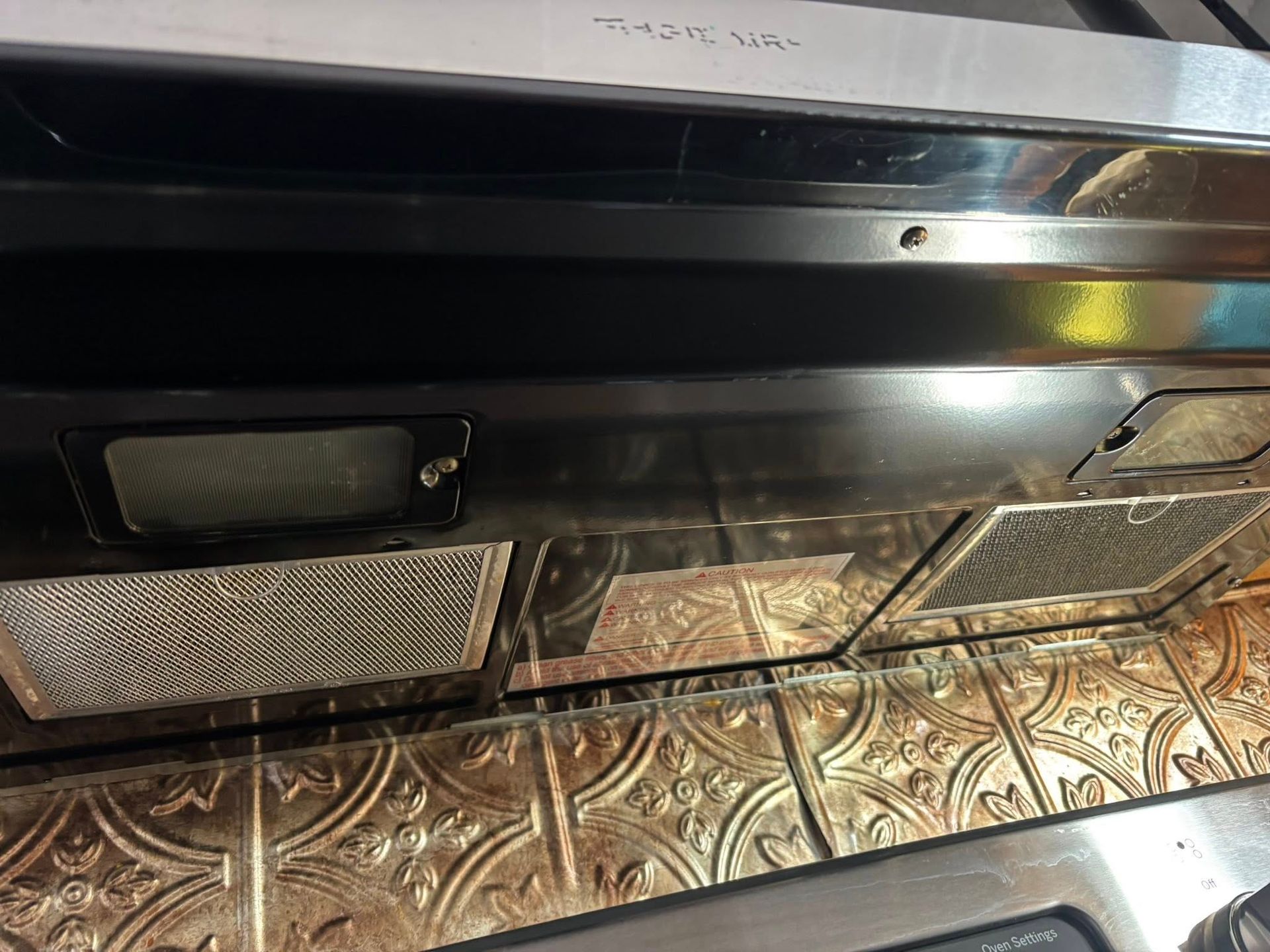 Underside of a black kitchen range hood featuring two rectangular metal grease filters above a textured metallic backsplash.