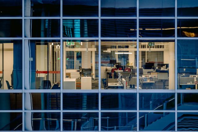 Office building window with illuminated workspaces, evening light.