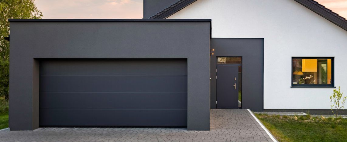 Modern black garage door set into a charcoal-gray extension on a contemporary white home.