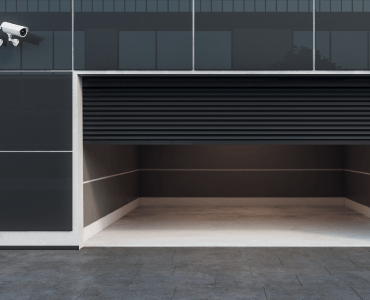 A security camera is mounted on the side of a building next to a garage door.
