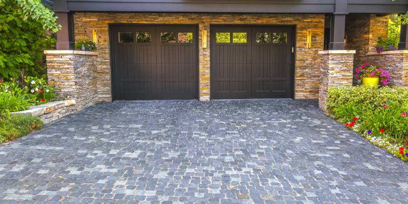 Elegant stone home featuring two dark brown garage doors, complemented by a textured cobblestone driveway.