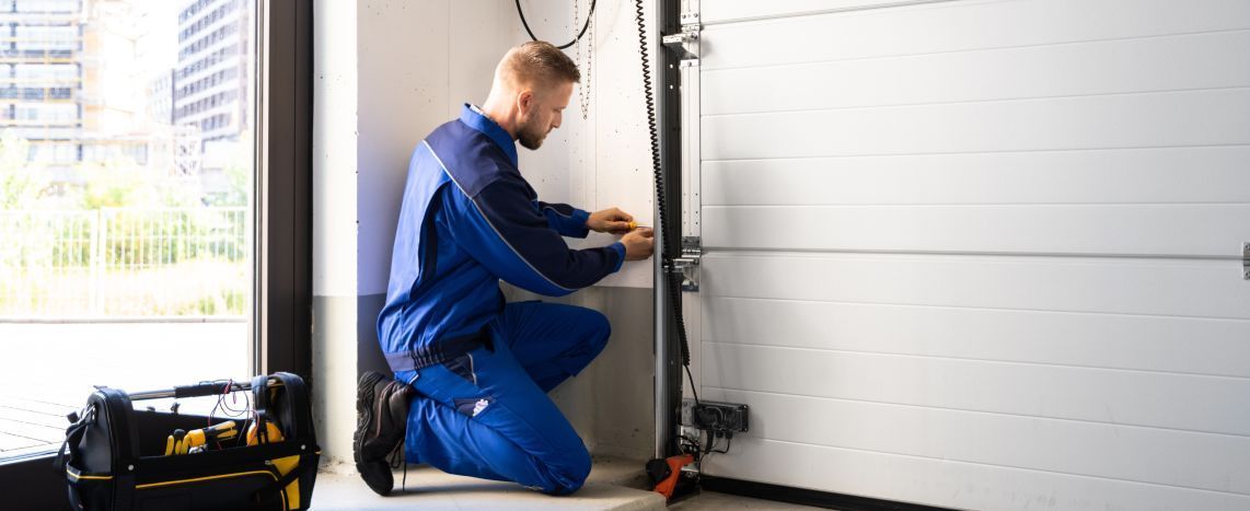 A man is kneeling down in a garage fixing a garage door.