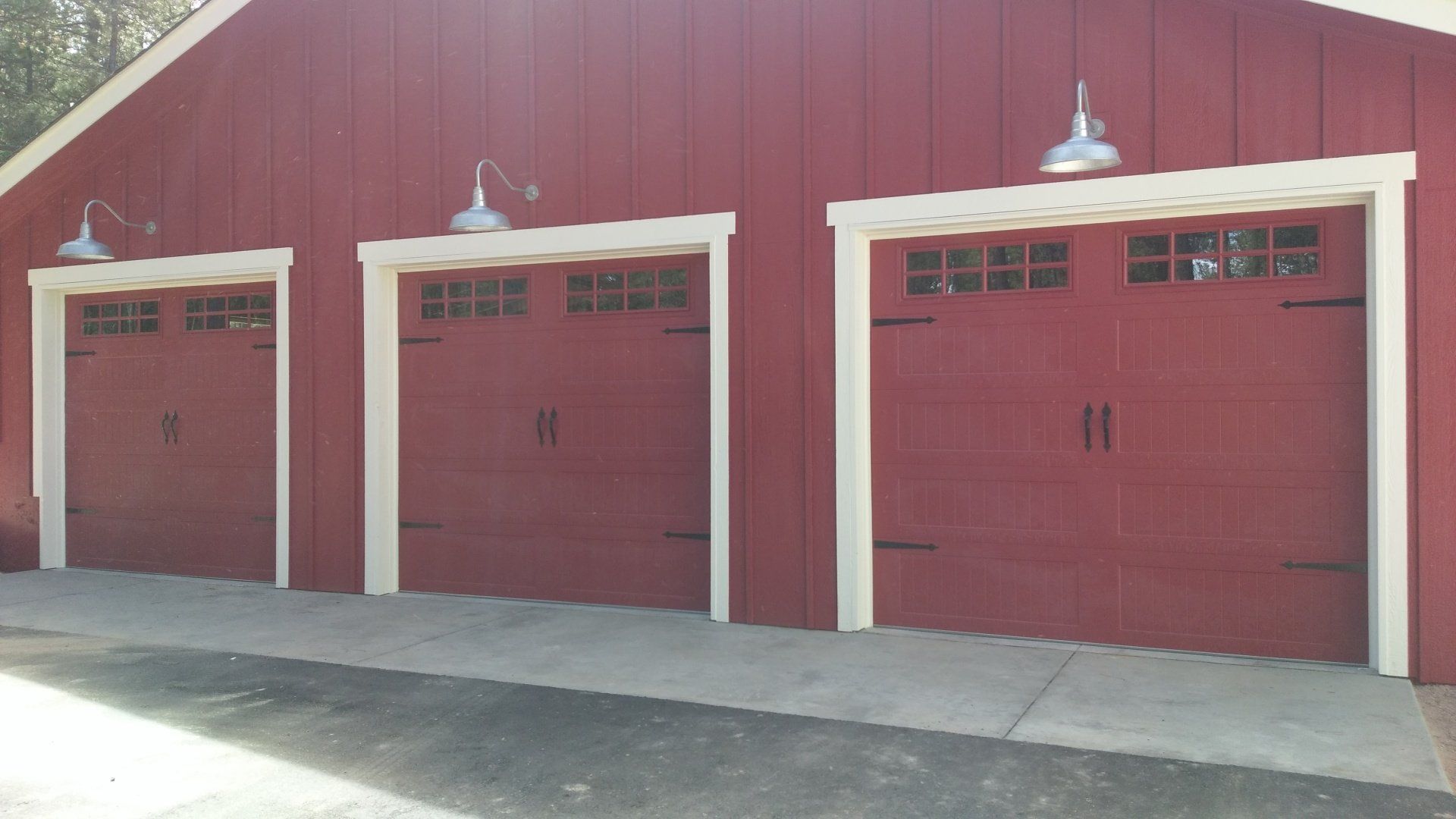 Red barn-style garage with three matching red doors featuring black hardware and upper window panels.
