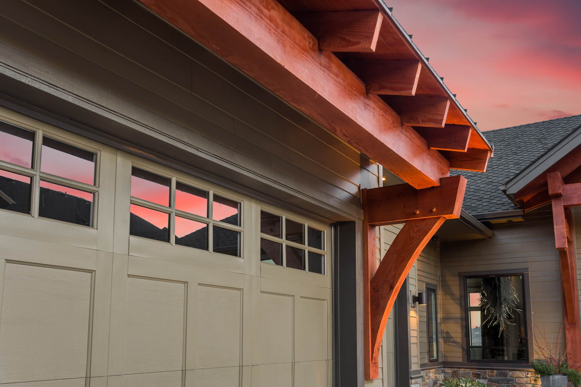 White garage doors with top-row windows beneath exposed wood beams on a Colorado home during sunset