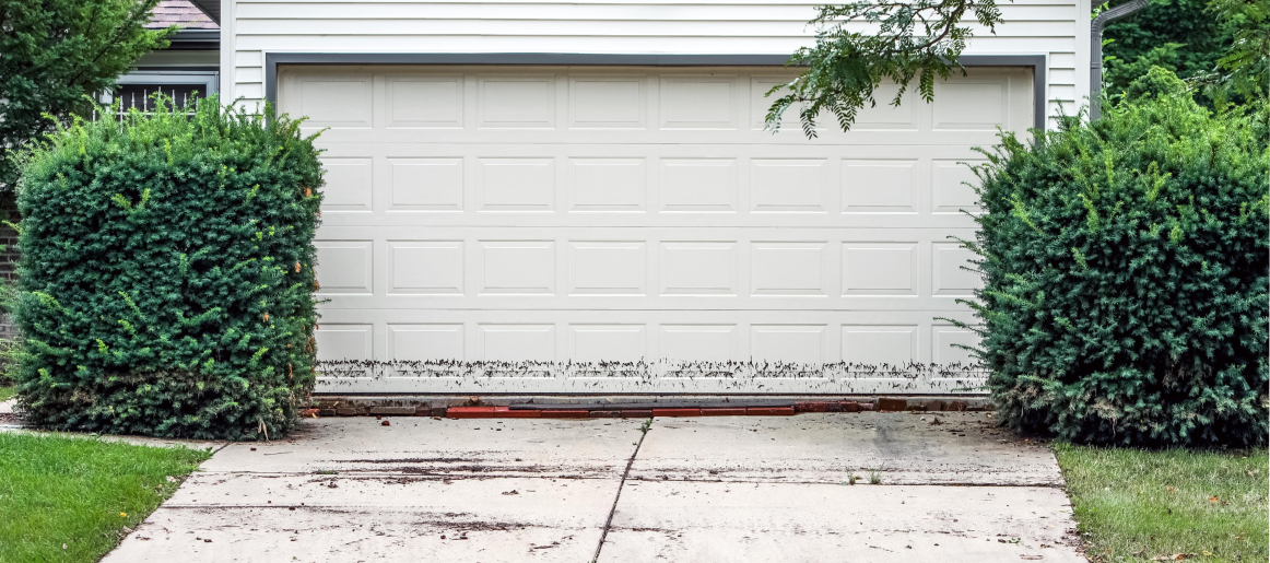 White garage door with water damage at the base, showing the need for storm prep or garage door weatherproofing services.