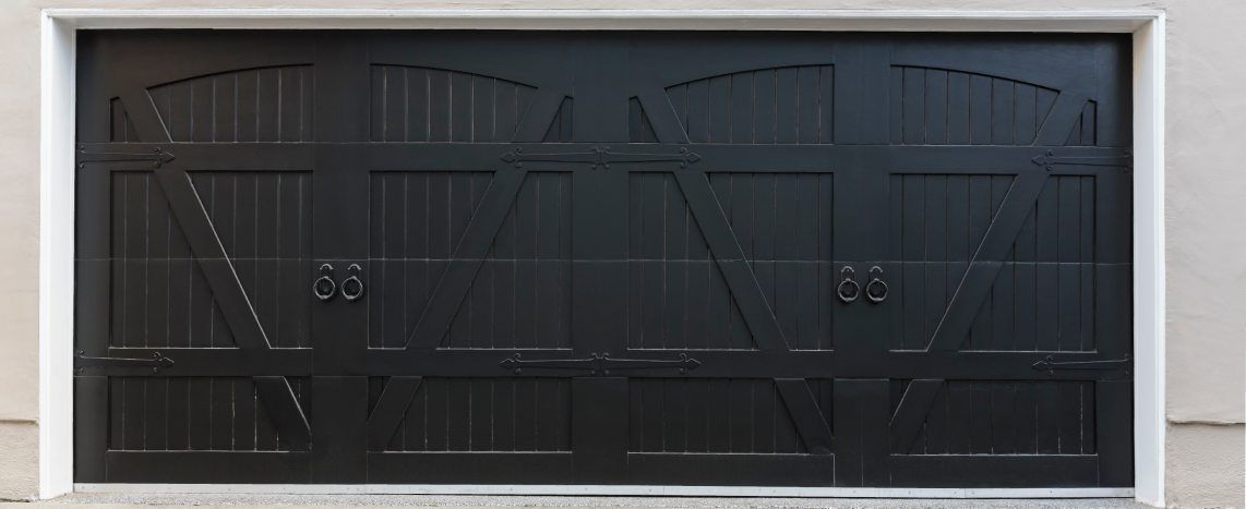 Black carriage-style garage door with decorative cross-bracing, vertical panels and ring handles.