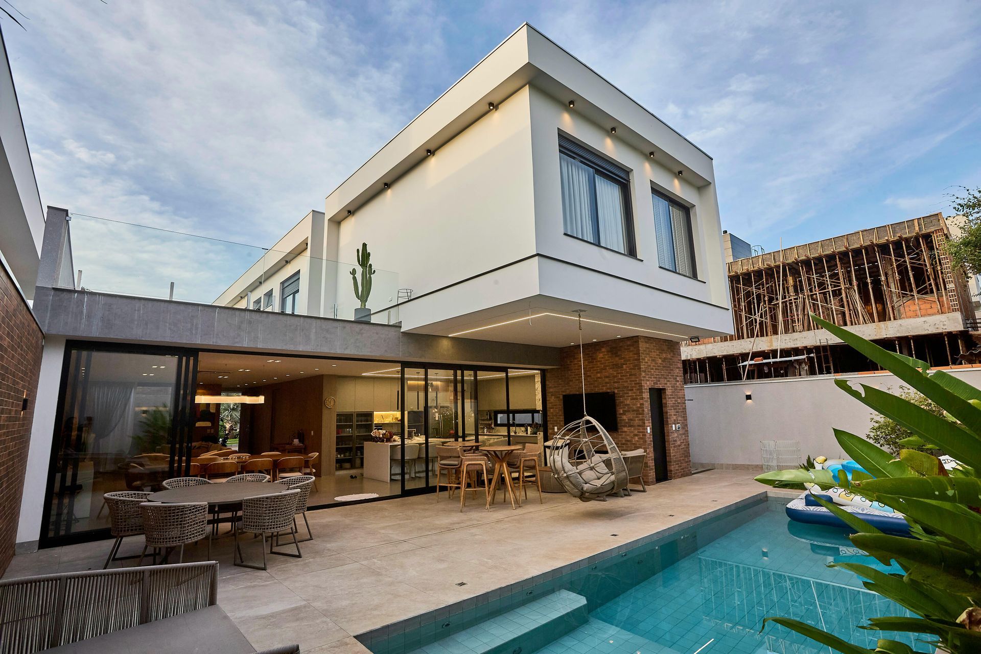 Modern two-story house with patio dining area and turquoise pool in a sunny backyard