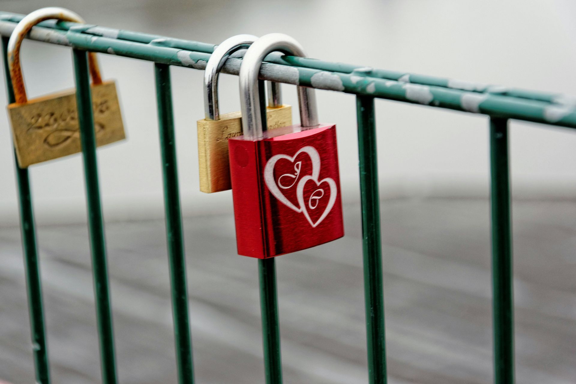 Several padlocks, including a red one with a heart, hang on a green metal railing.