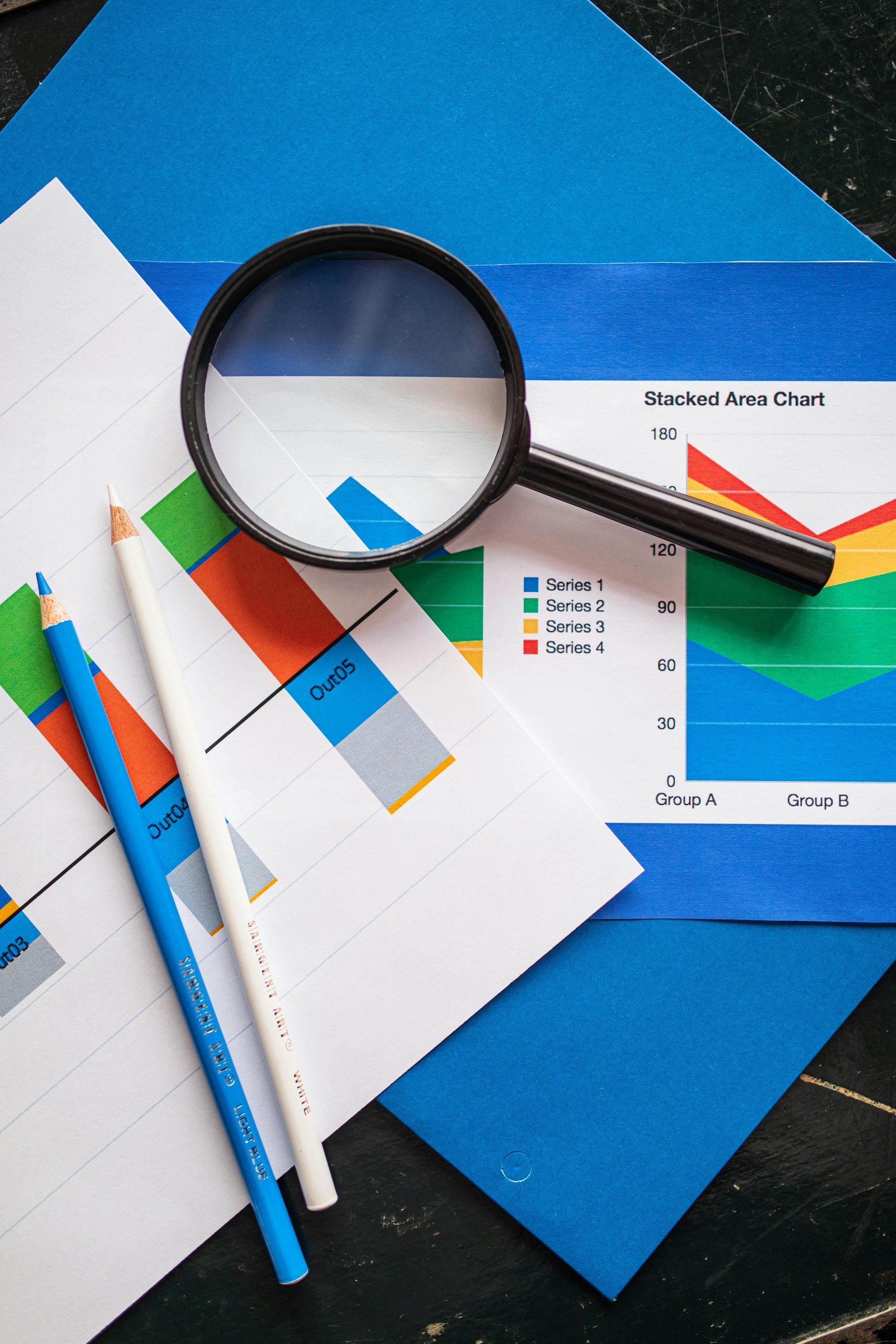 Magnifying glass over colorful charts, graphs, and pens on a blue desk