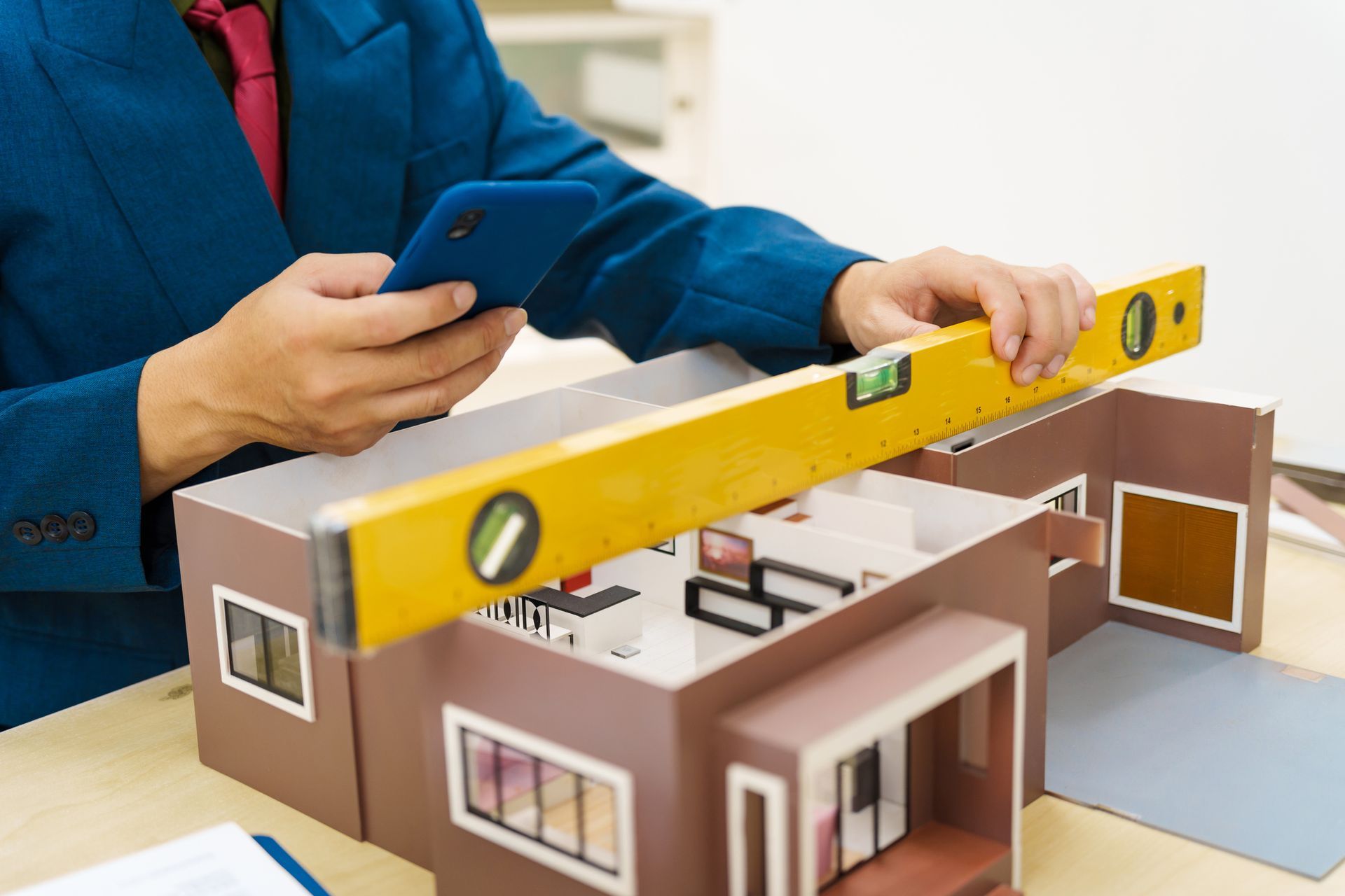 A man is using a level to measure the height of a model house.