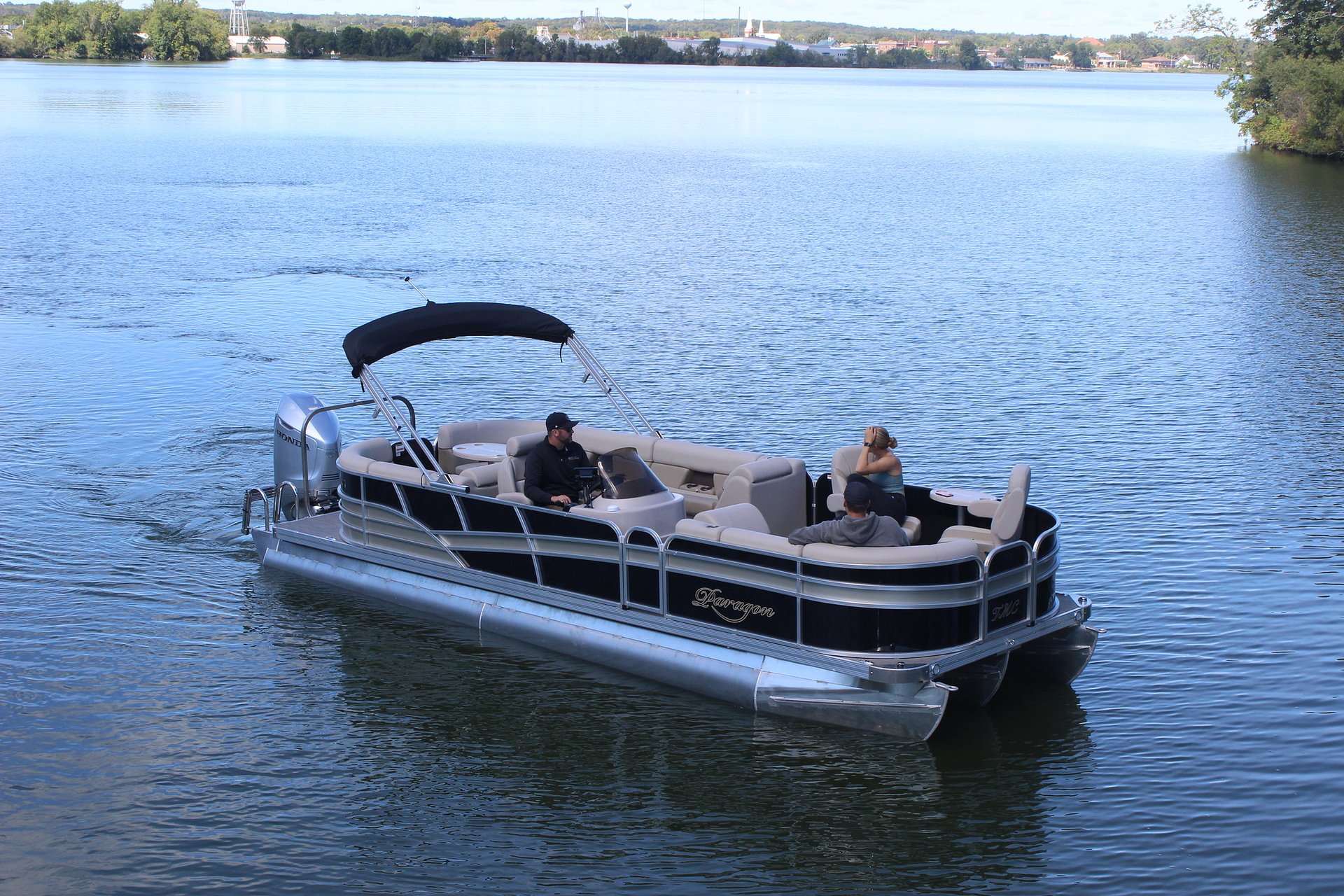 Pontoon boat on dry land, blue and silver, with canopy, trees in background.