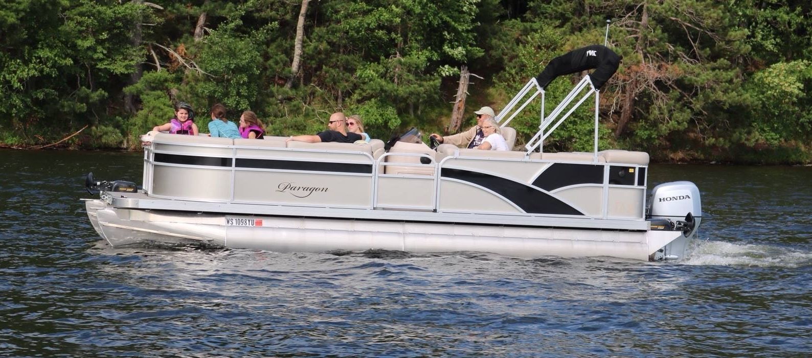 Interior of a pontoon boat with tan seating, overlooking a lake with trees in the background.