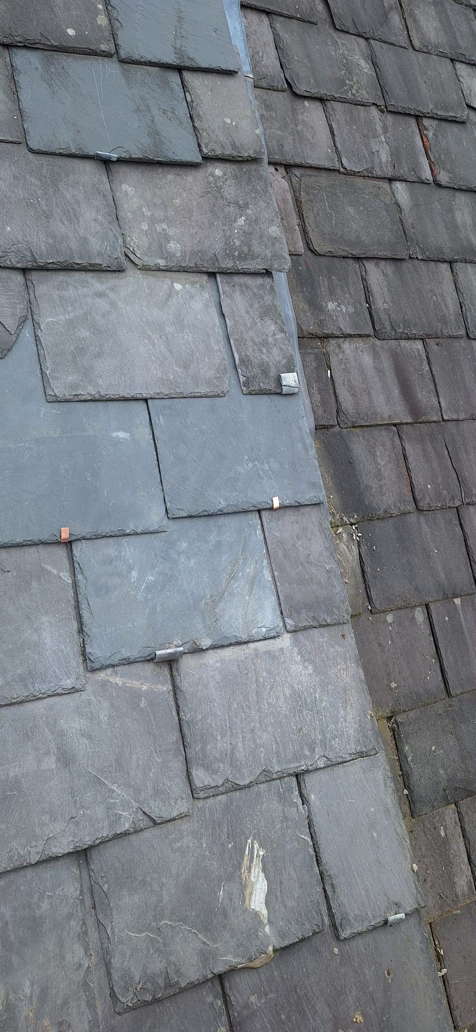 Close-up of weathered gray roof slates with a vertical seam and slight discoloration