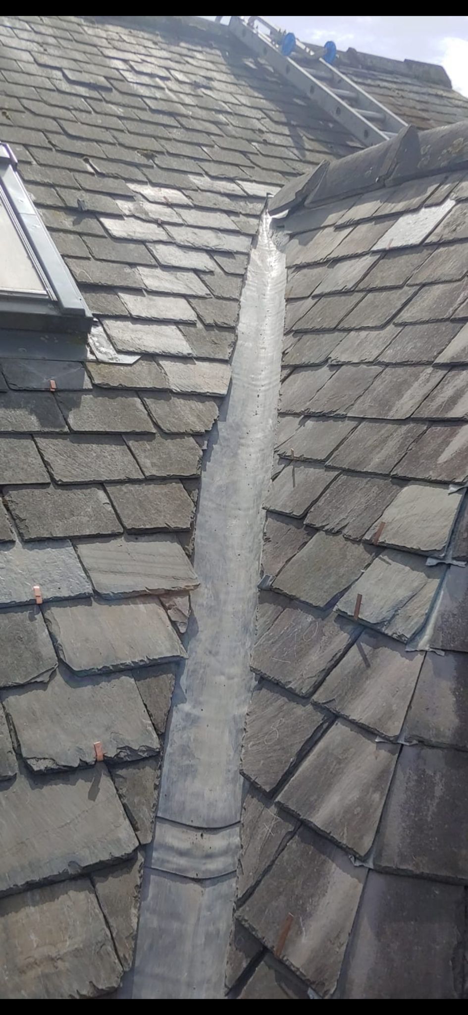 A close up of a roof with slate tiles and a skylight.