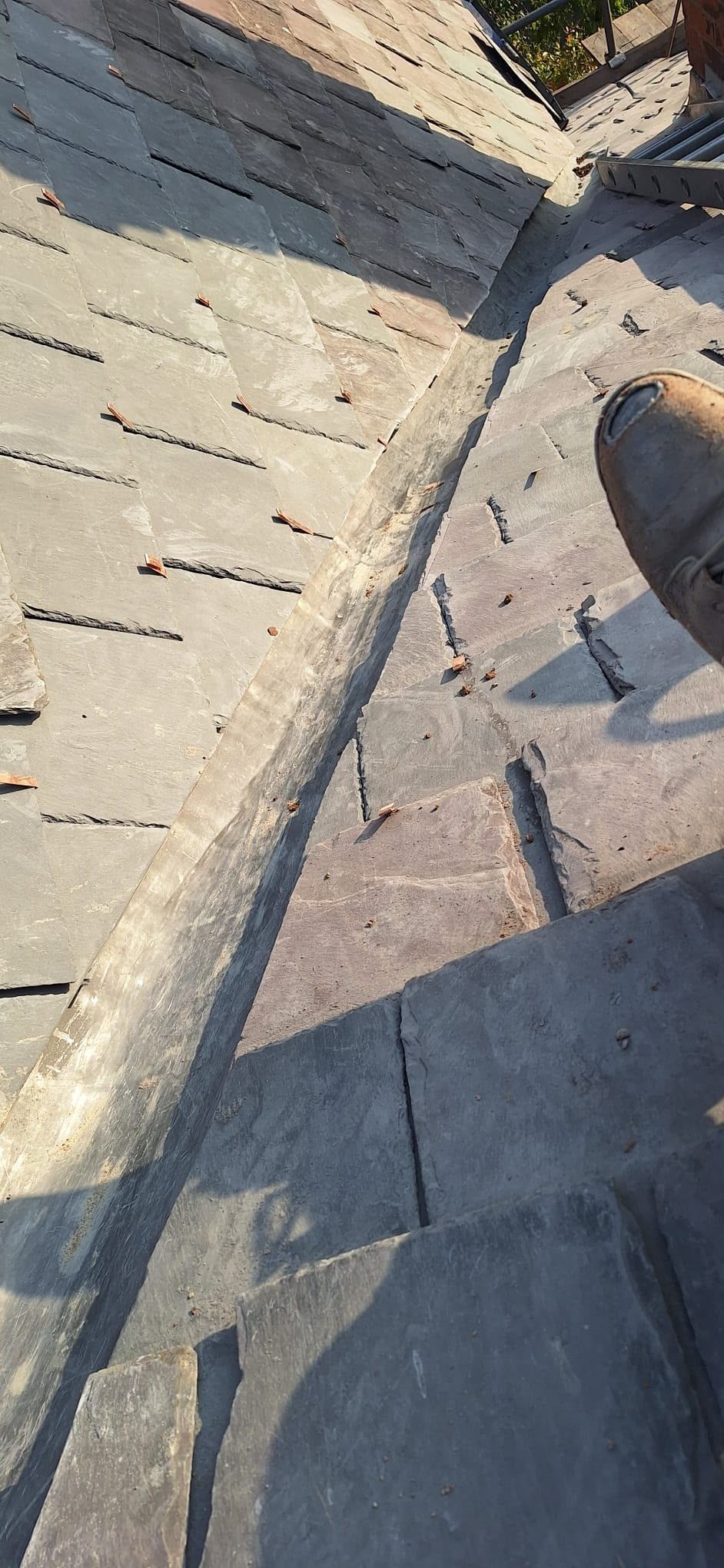 Close-up of weathered gray roof shingles with a central ridge seam and scattered debris