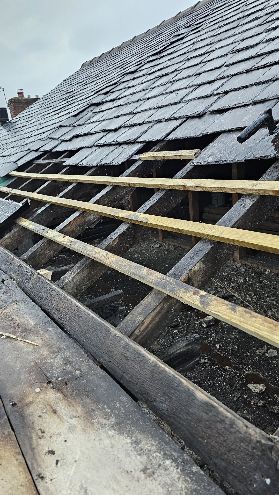 Damaged roof with missing slate tiles, showing wooden rafters.