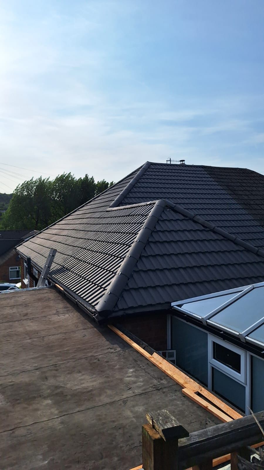 Dark roof tiles on a house, viewed from a flat roof. Blue sky in background.