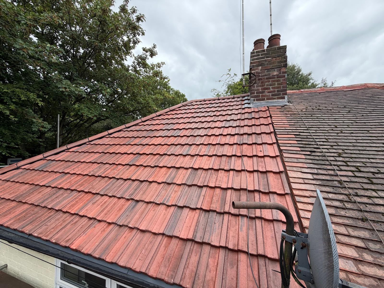 Red tiled roof with chimney, overcast sky, and trees in the background