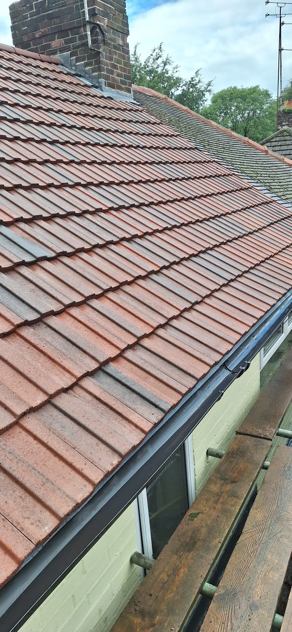 Red clay-tiled roof with a sloped skylight and gutter beside a house wall