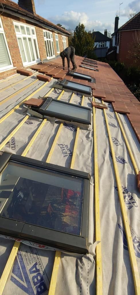 Rooftop under construction with skylights, insulation panels, and a worker walking along the roofline