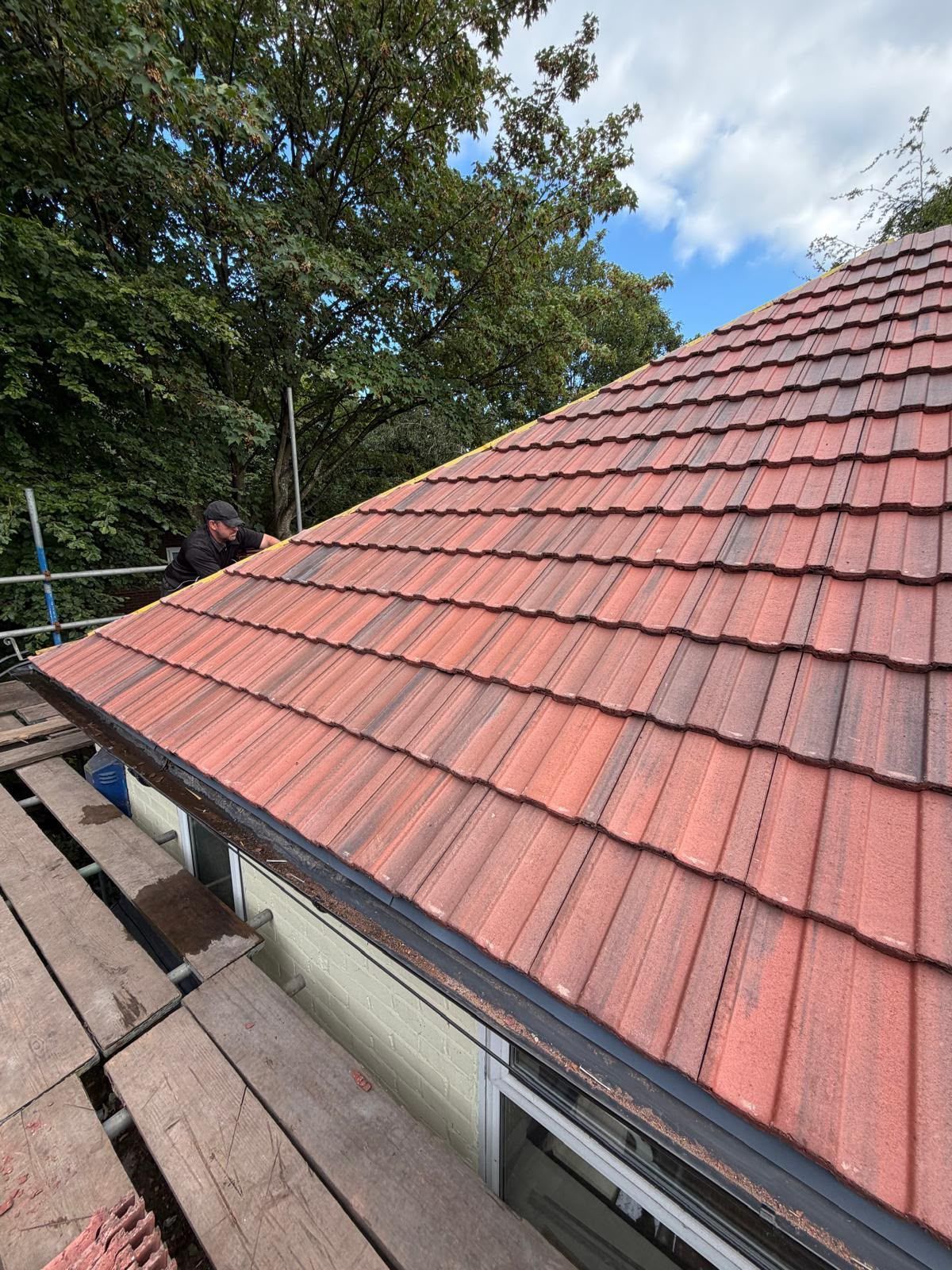 Red tiled roof beside a sloped shingle roof, with trees and blue sky in the background