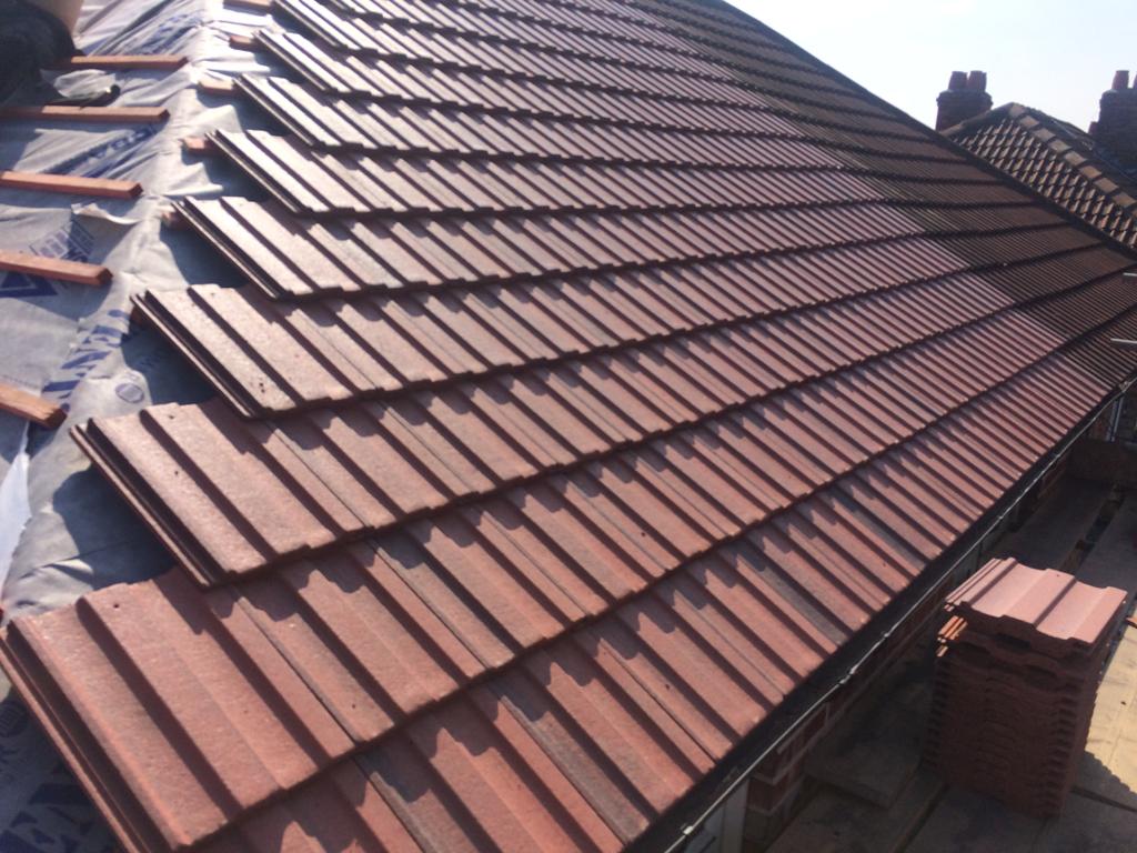 A picture of a red concrete tile hipped roof being replaced by Roofers Manchester