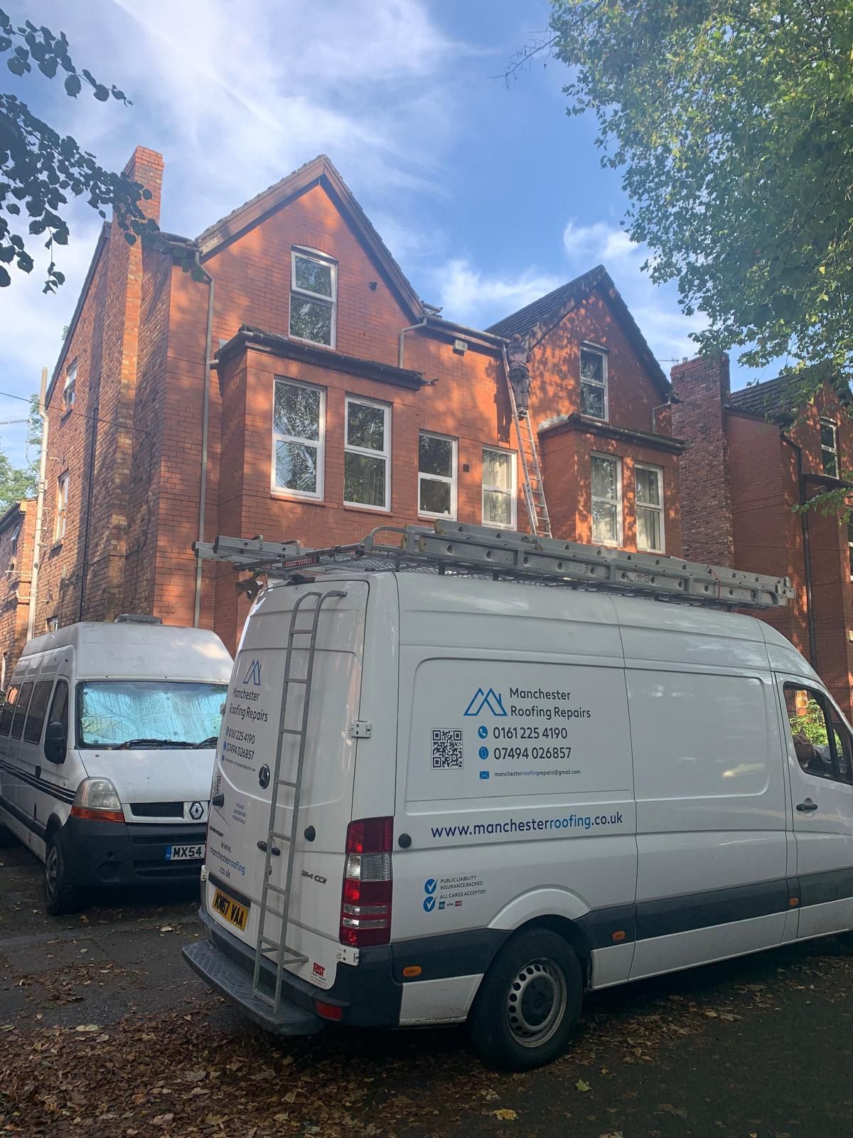 Two white vans are parked in front of a large brick building.