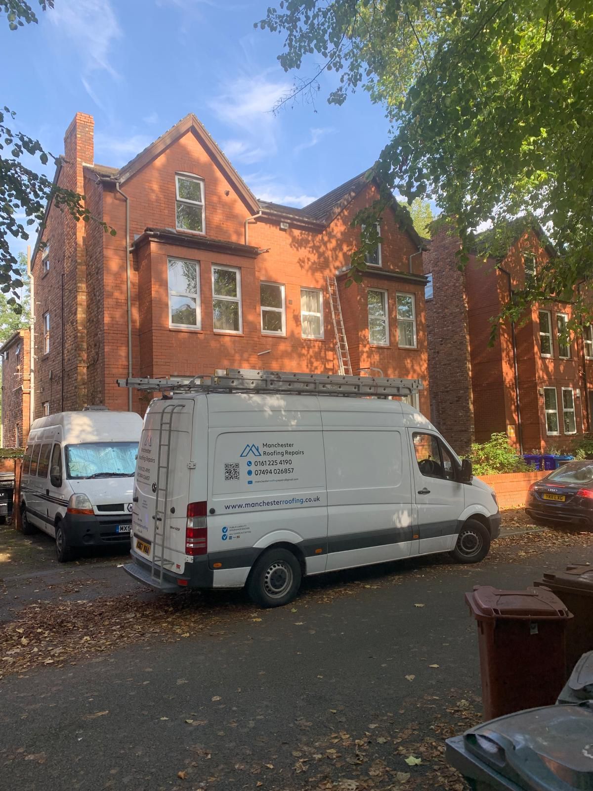 The white Manchester Roofing Repairs van is parked in front of a large brick building.