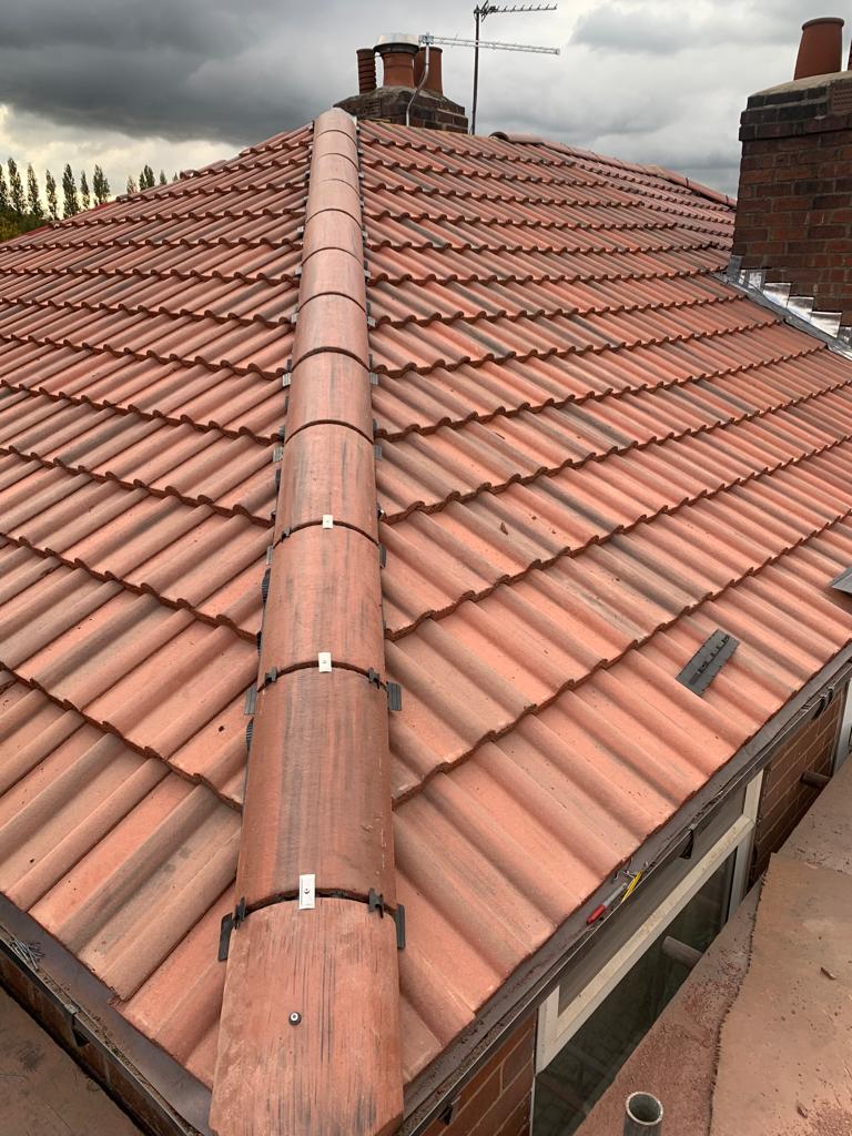 A picture of a concrete tile hipped roof in dark red by Roofers Manchester