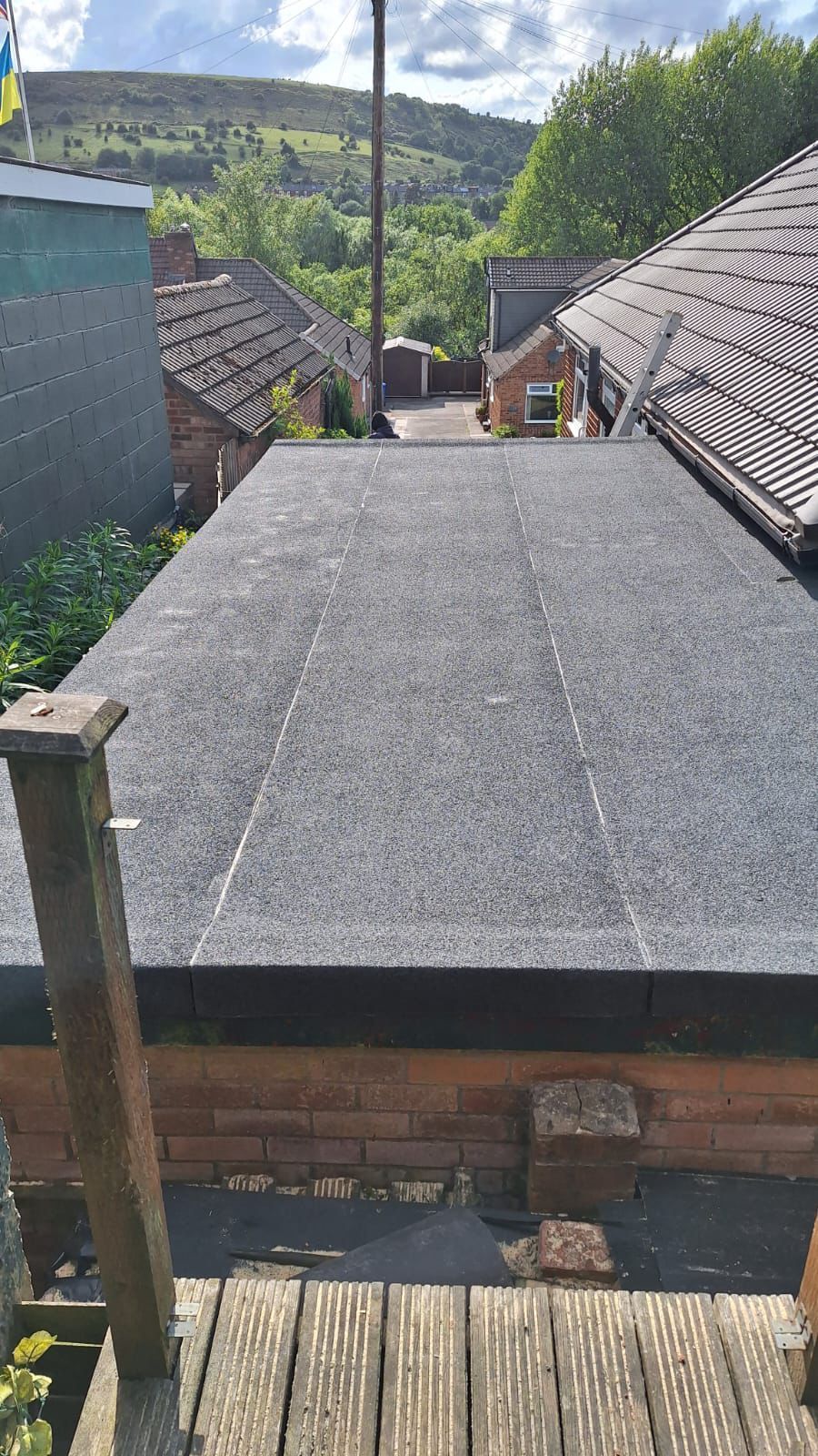Flat felt roof in a village, with hills and trees in the background.