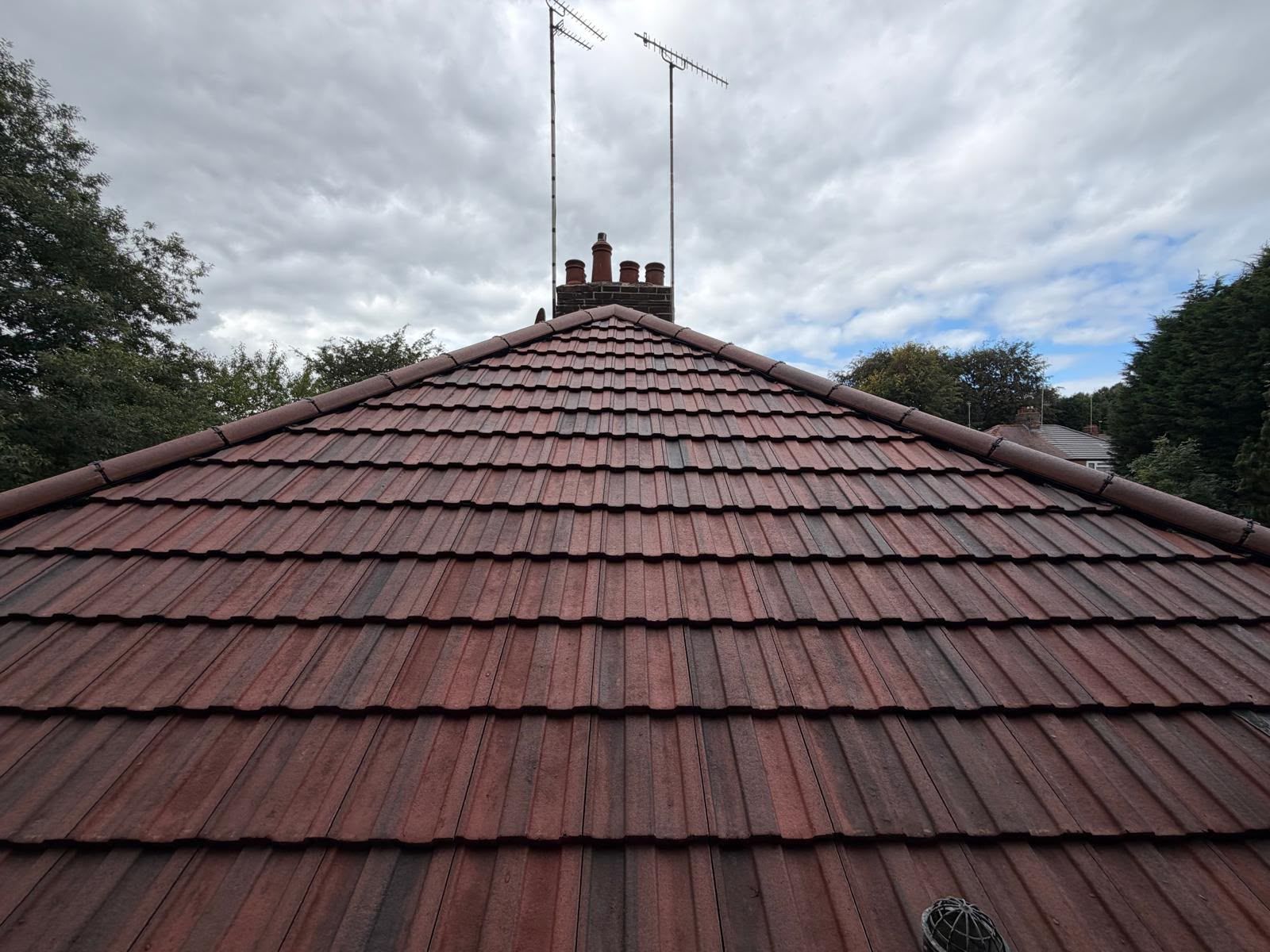 Red tiled roof with two TV antennas under a cloudy sky