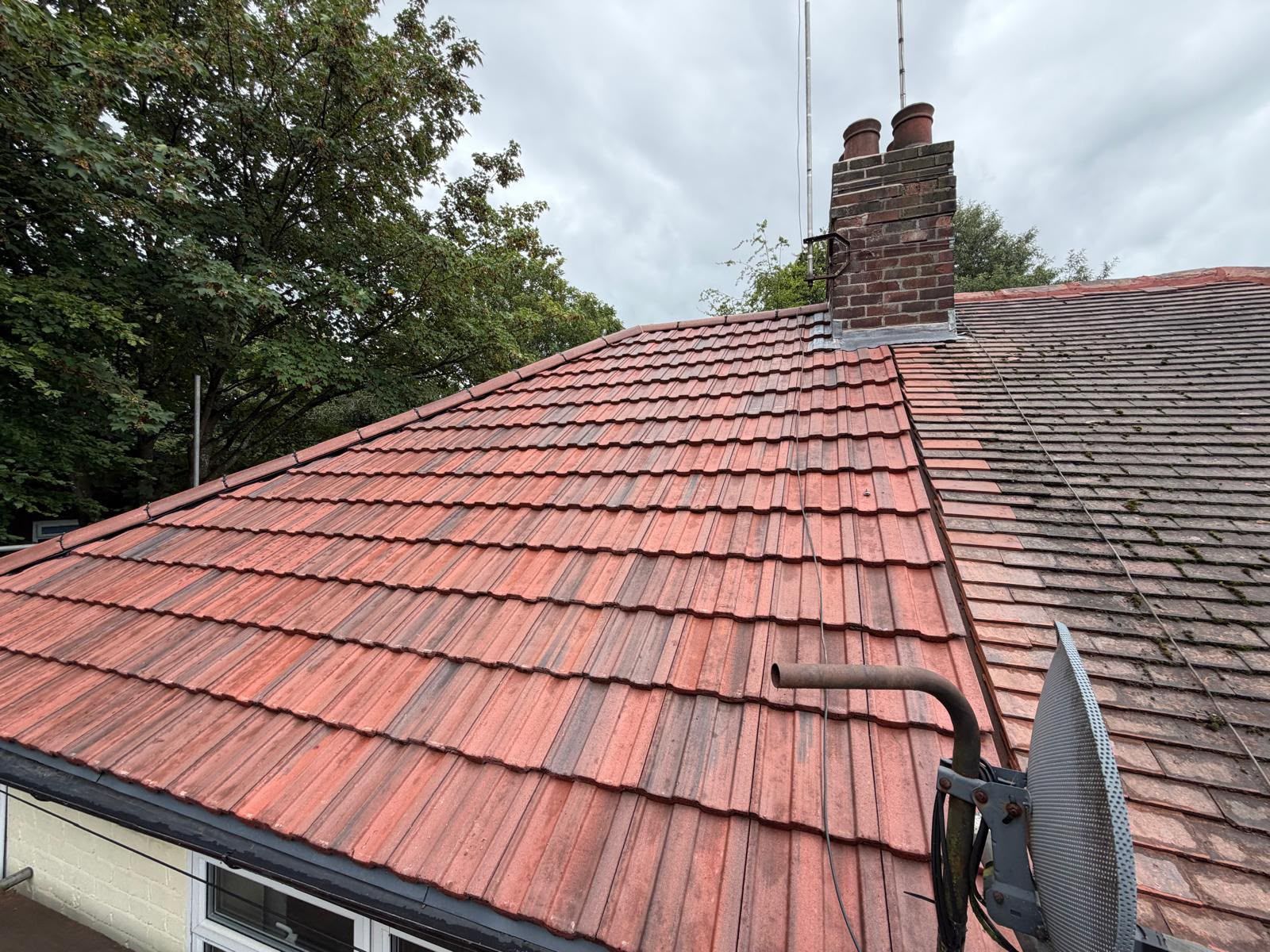 Red tiled roof with a ridge seam beside a darker roof and brick chimney under cloudy sky
