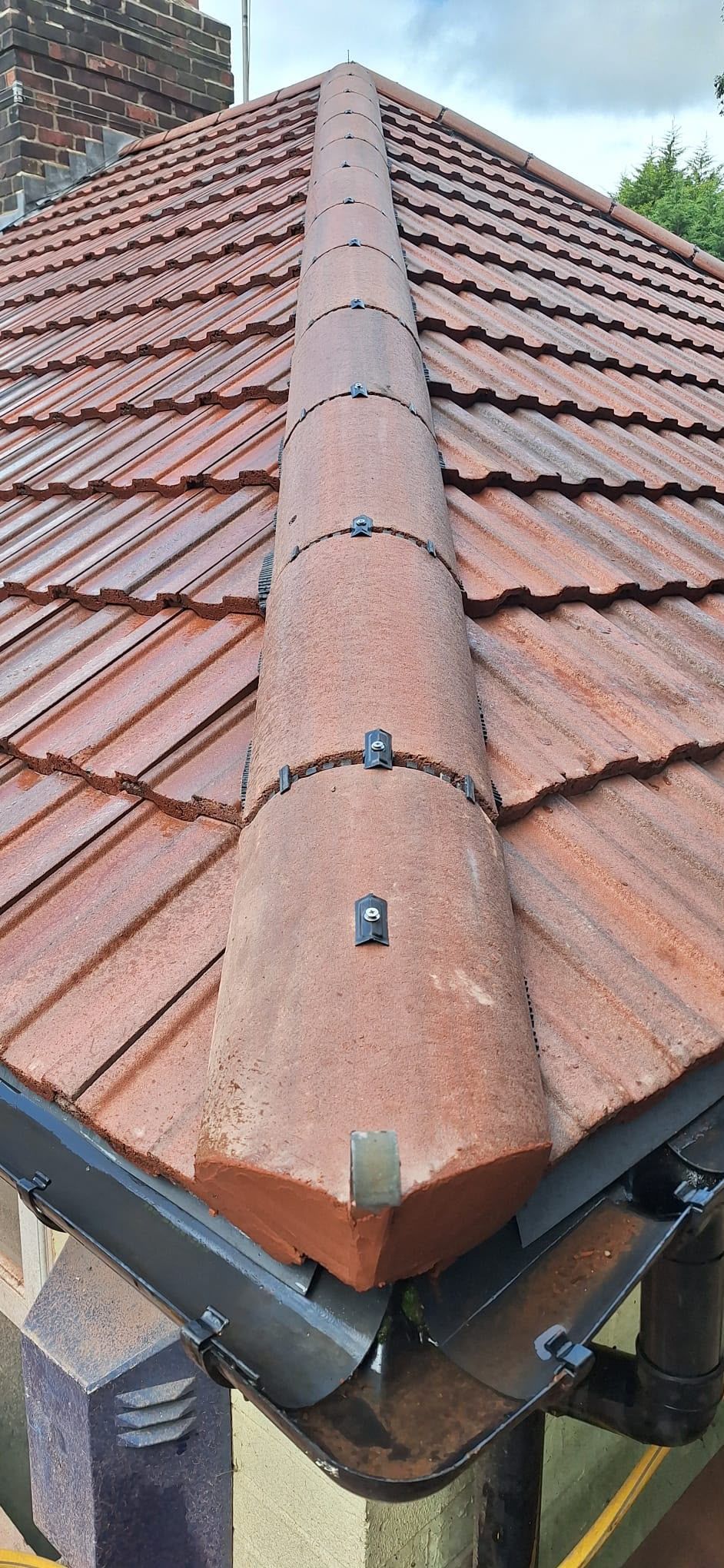 Reddish tiled roof with a central ridge vent or chimney flashing against the sky