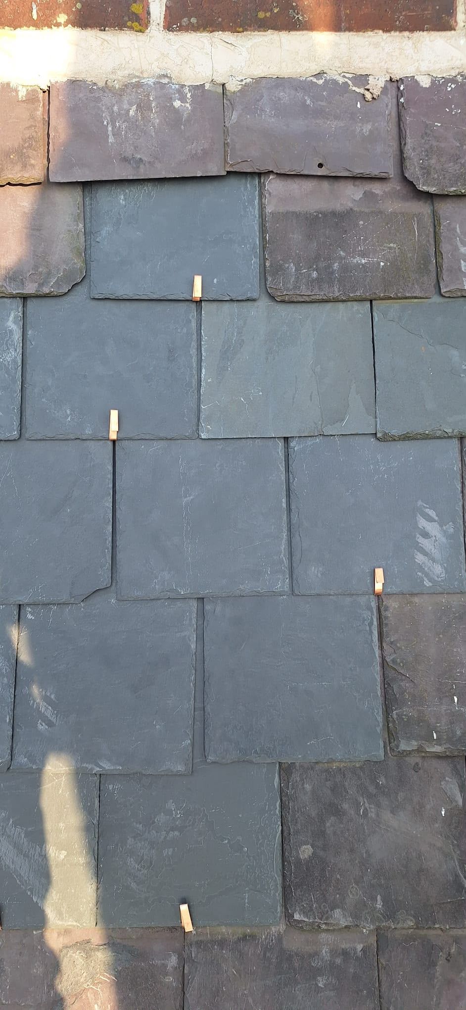 Blue-gray roof slates beneath a row of weathered brown slates and brick trim