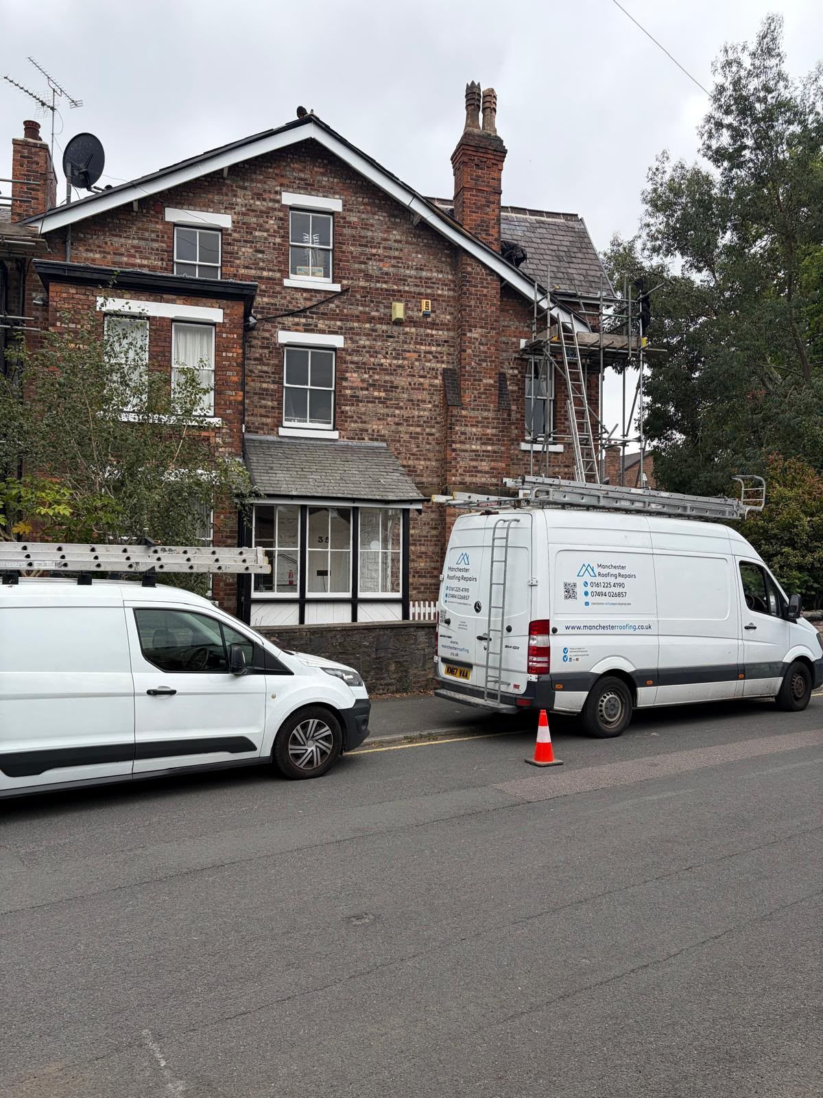 Brick house with white vans and traffic cone parked on a residential street.