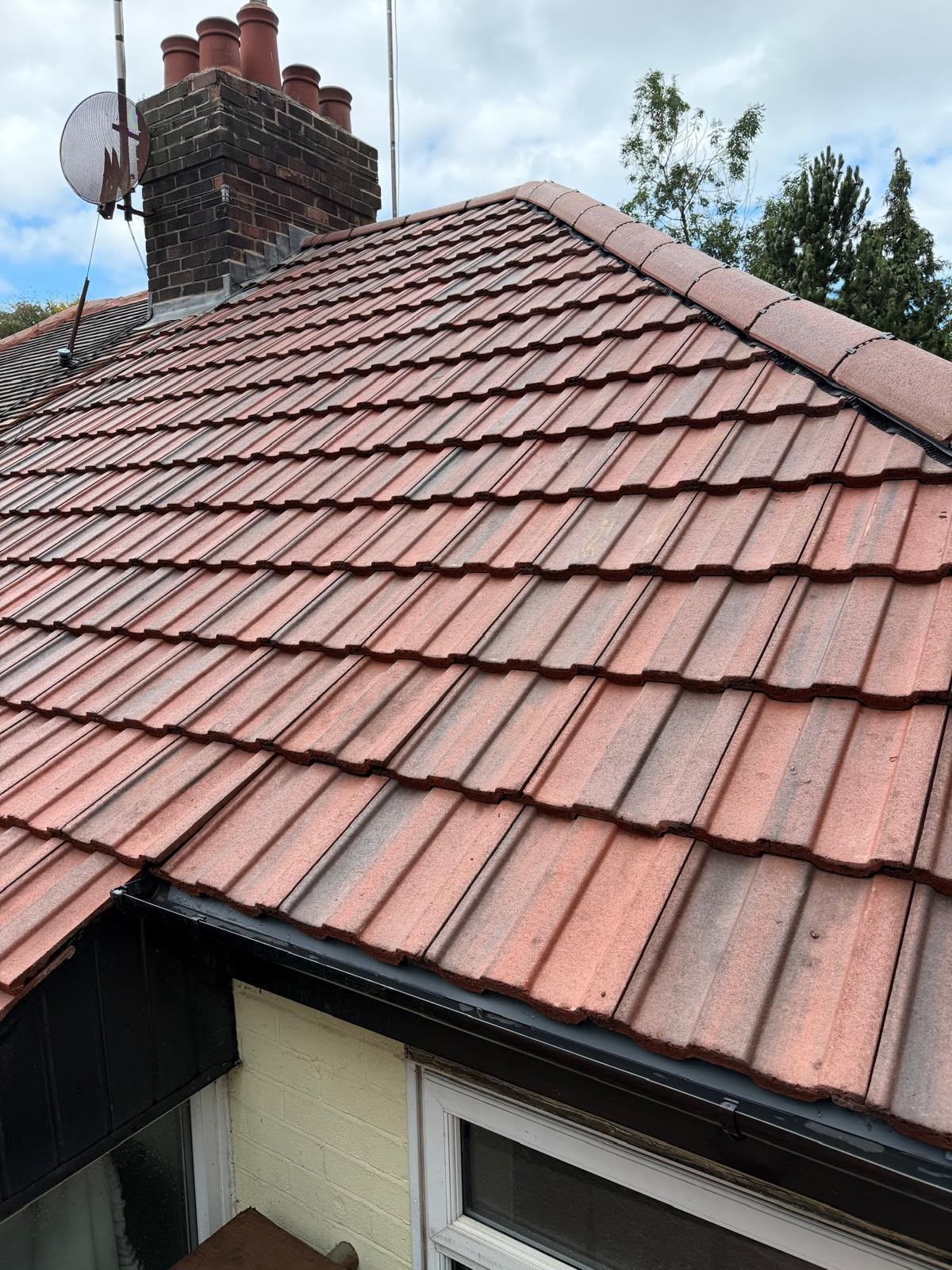 Red tiled roof with chimney and satellite dish above a house window