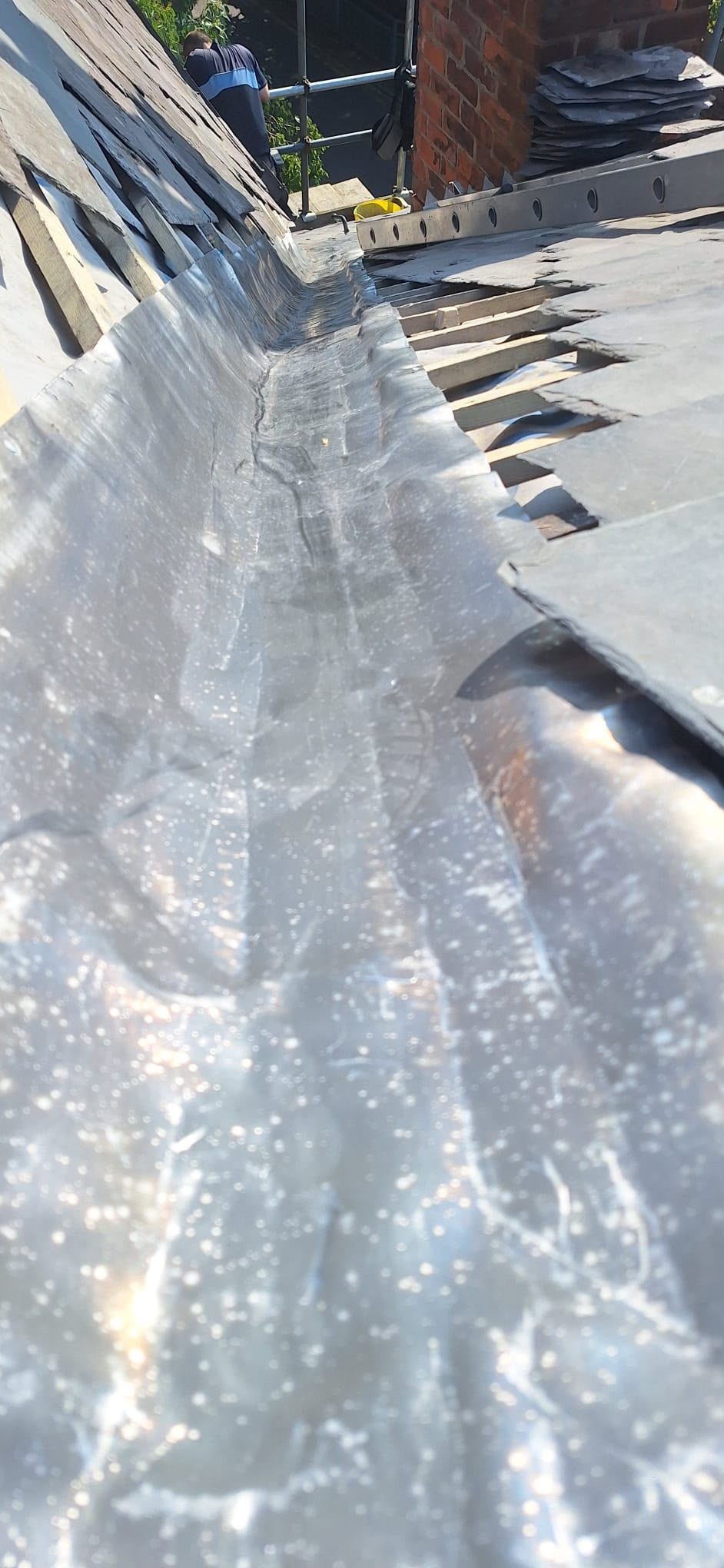 Clear plastic sheeting stretched along a sunlit rooftop beside a brick wall