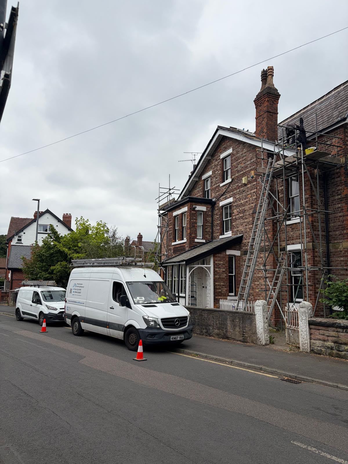 Manchester Roofing Repairs white vans parked on a residential street beside a brick house with road