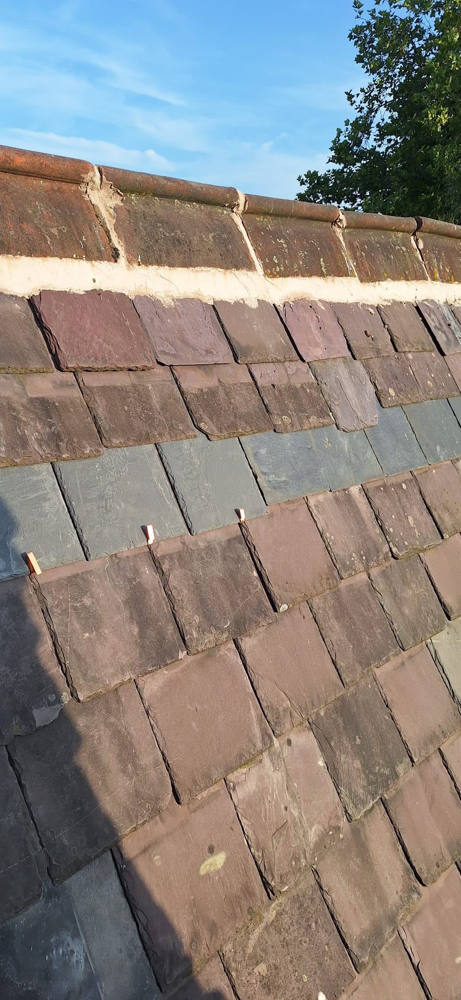 Close-up of a sloped roof with weathered brown and gray shingles under a blue sky