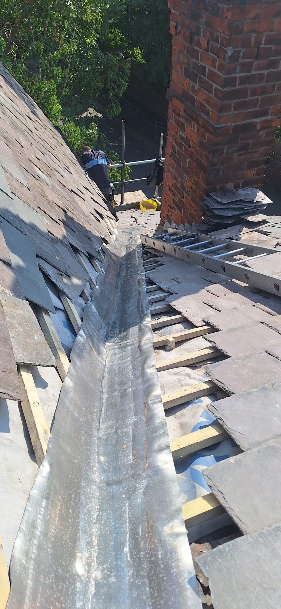 Close-up of a damaged roof valley with missing shingles and exposed underlayment near a brick chimney