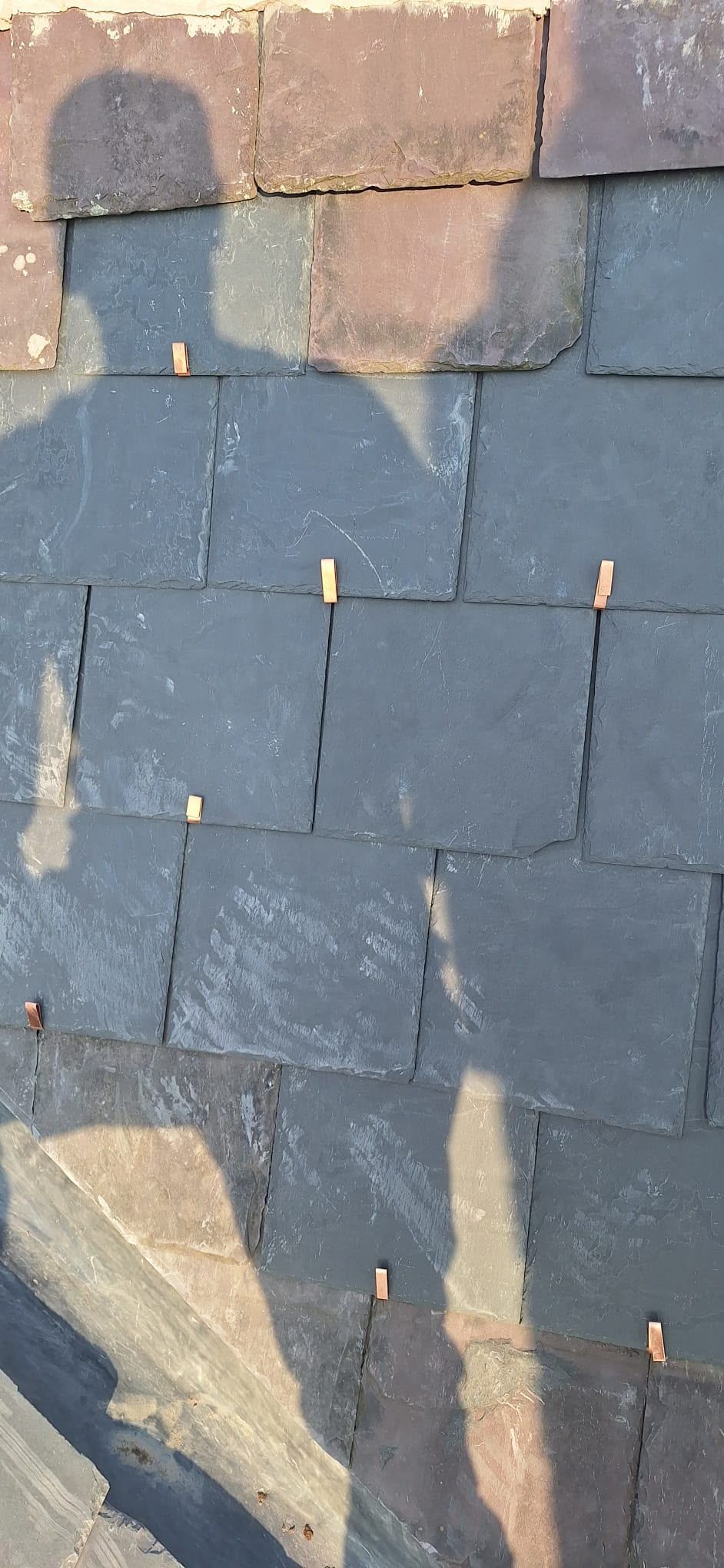 Shingle roof with a person’s shadow cast across gray and tan tiles
