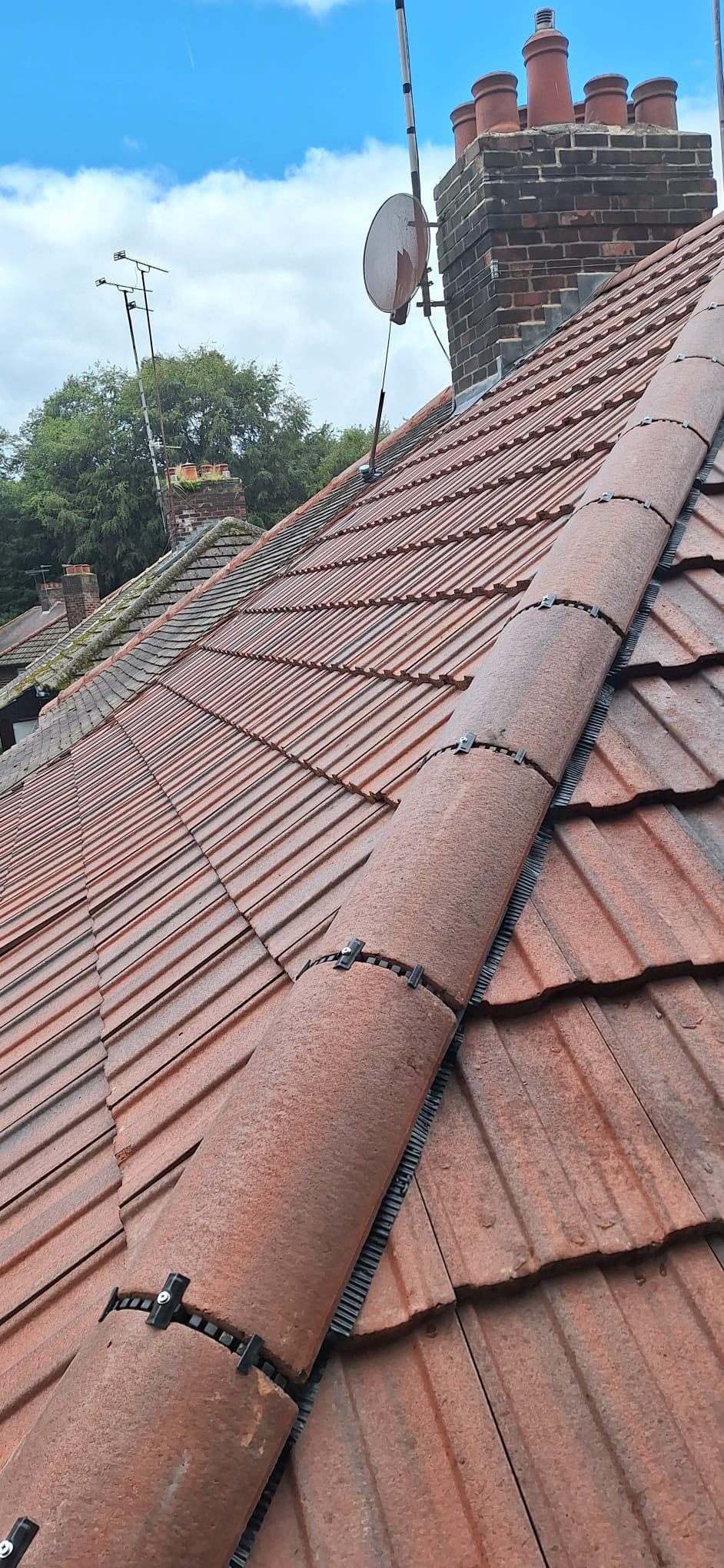 Red tiled roof with chimney stacks and a satellite dish beside a house under a cloudy sky
