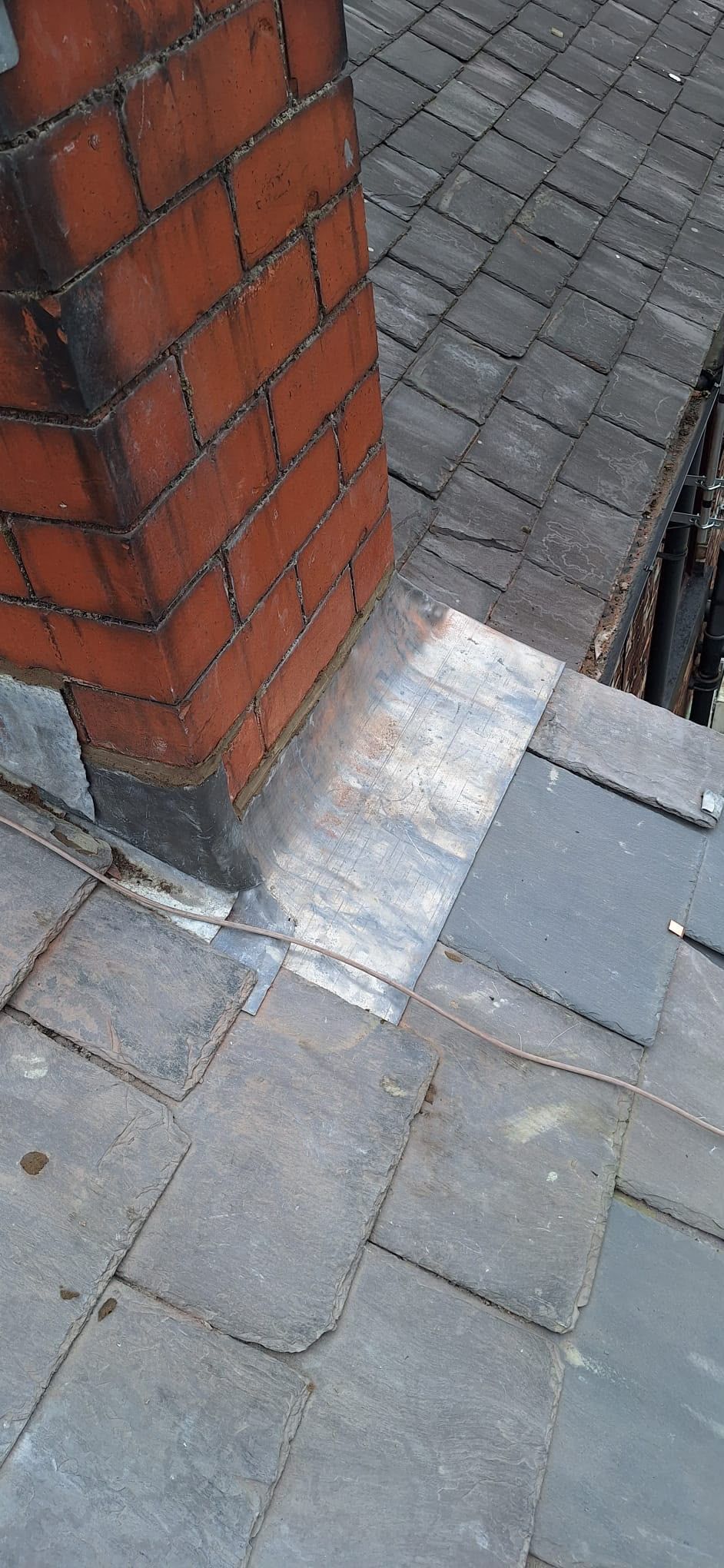 Close-up of a brick pillar beside gray roof slates and a lead flashing seam
